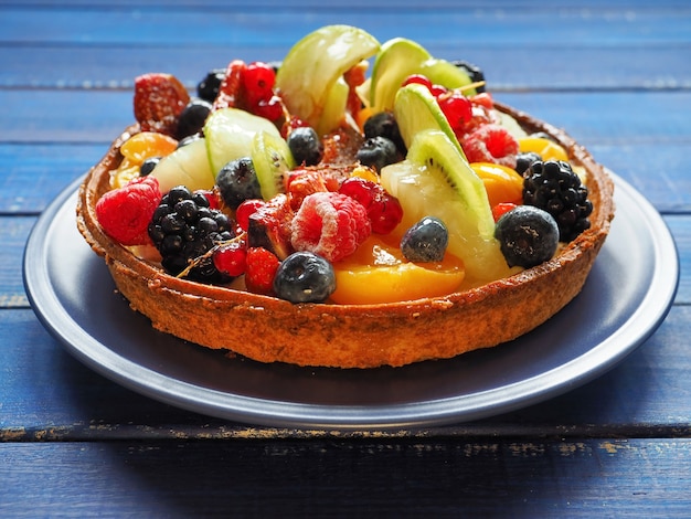 Delicious tart with exotic fruits and berries on blue wooden surface