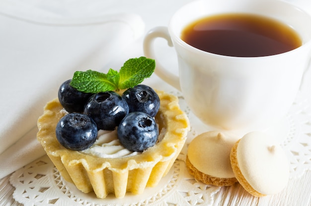 Delicious tartlet with fresh blueberries and cream cheese, a cup of tea and small cookies.