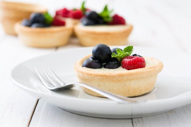 Delicious tartlets with raspberries and blueberries on white wooden table