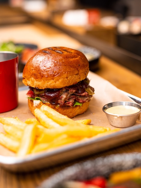 Delicious tasty grilled home made burger with beef,cheese,bacon and sauce on wooden table with copy space. Hands holding burgers with french fries and beer. Group of friends eating fast food