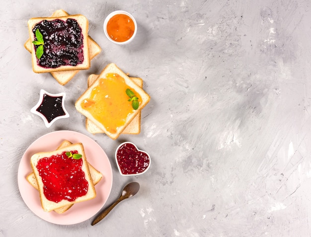 Delicious toasts with various sweet jams on grey background. Copyspace for your text, banner.