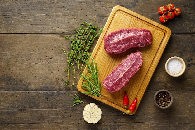 Delicious two raw top blade beef steak on wooden board with spices and herbs