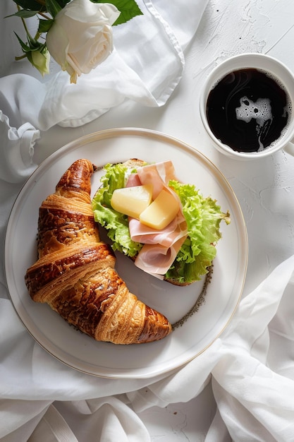 Delight in a croissant sandwich with ham cheese and salad paired with coffee on a pristine white