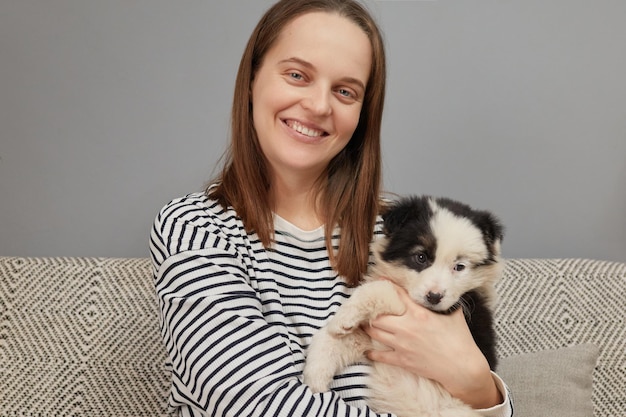 Delighted attractive happy Caucasian woman wearing striped shirt sitting on couch with black and whi