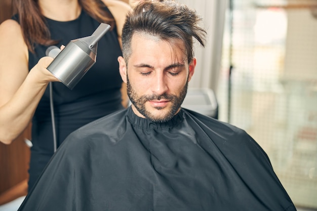 Delighted brunette man keeping eyes closed while waiting for hairstyle