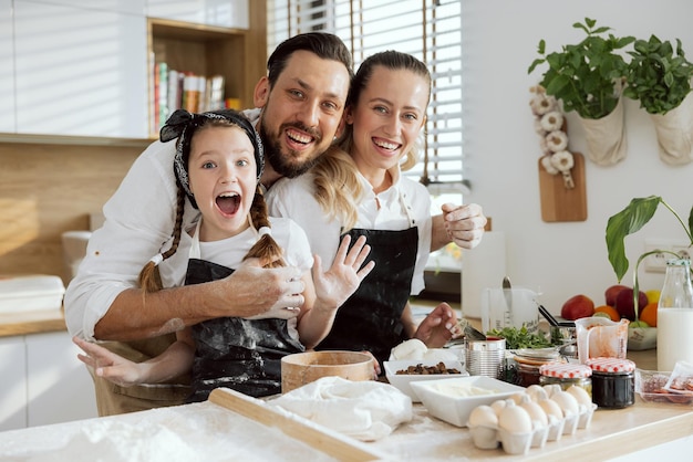 Delighted child having fun with parents cooking baking homemade domestic pizza