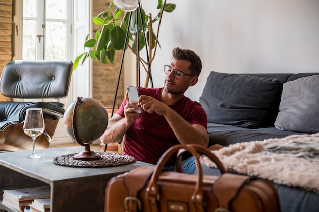 Delighted male traveler choosing country on planet Earth globe before adventure while sitting in room with suitcase