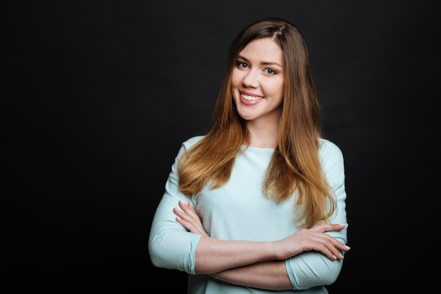 Delighted optimistic young woman smiling and expressing joy while standing isolated in black wall