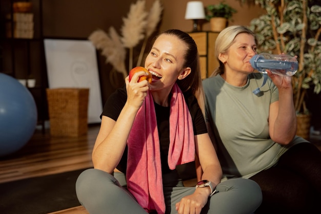 Delighted young girl biting ripe apple after workout with elderly mother