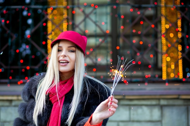 Delightful blonde model celebrating New Year with sparklers at the blurred city lights. Space for text