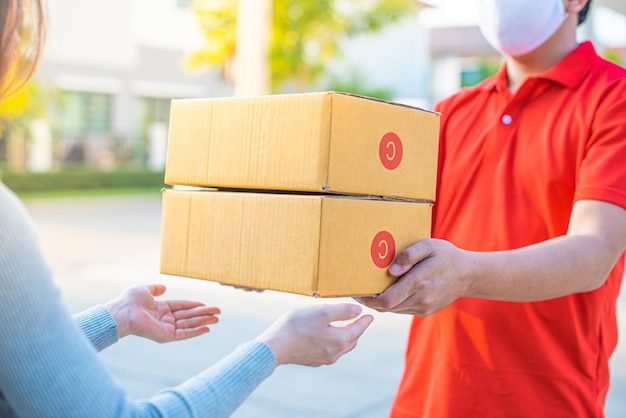 Deliver man wearing face mask in red uniform handling bag and parcel box give to female costumer