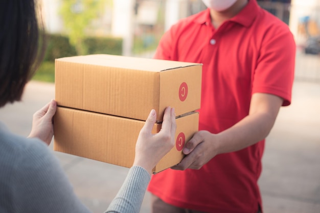 Deliver man wearing face mask in red uniform handling bag and parcel box give to female costumer