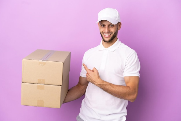 Delivery caucasian man isolated on purple background pointing back