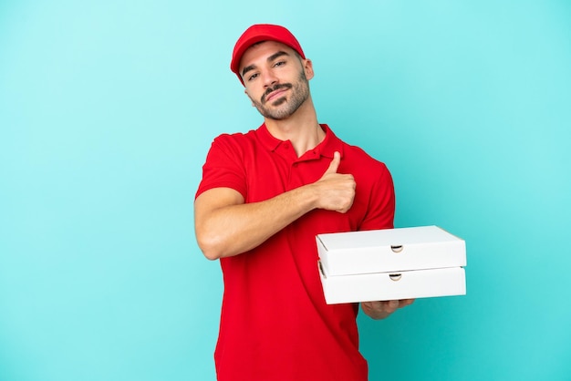 Delivery caucasian man picking up pizza boxes isolated on blue background giving a thumbs up gesture