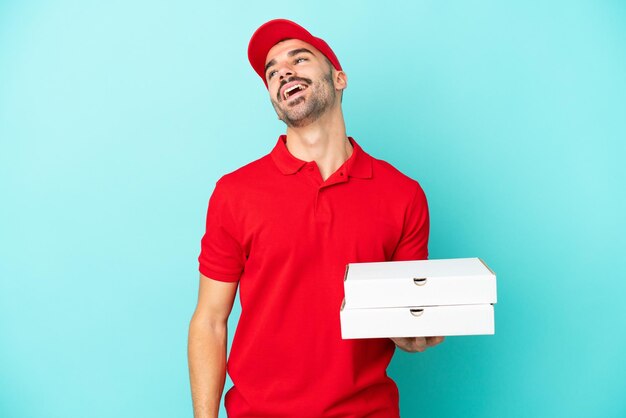 Delivery caucasian man picking up pizza boxes isolated on blue background laughing