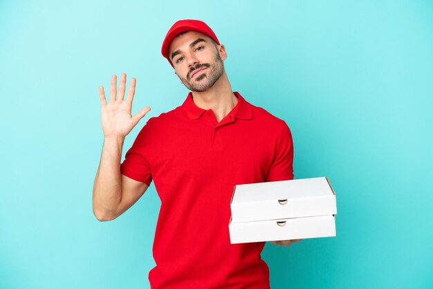 Delivery caucasian man picking up pizza boxes isolated on blue background saluting with hand with happy expression