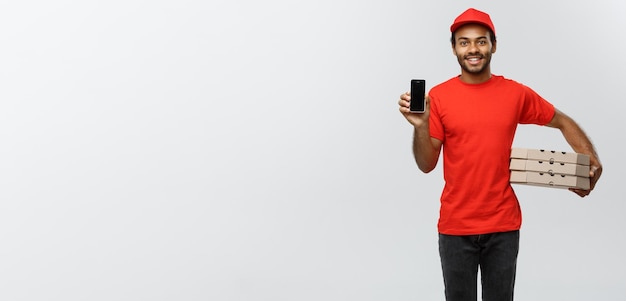 Delivery Concept Portrait of Handsome African American delivery man or courier with pizza box showing mobile phone on you to check the order Isolated on Grey studio Background Copy Space