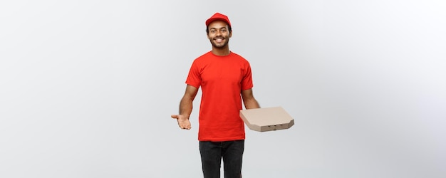 Delivery Concept Portrait of Happy African American delivery man pointing hand to present a pizza box package Isolated on Grey studio Background Copy Space