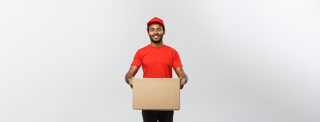 Delivery Concept Portrait of Happy African American delivery man in red cloth holding a box package Isolated on Grey studio Background Copy Space