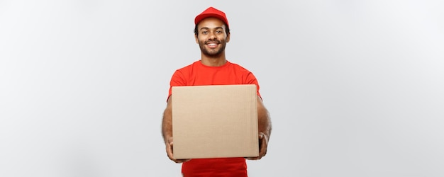 Delivery Concept Portrait of Happy African American delivery man in red cloth holding a box package Isolated on Grey studio Background Copy Space