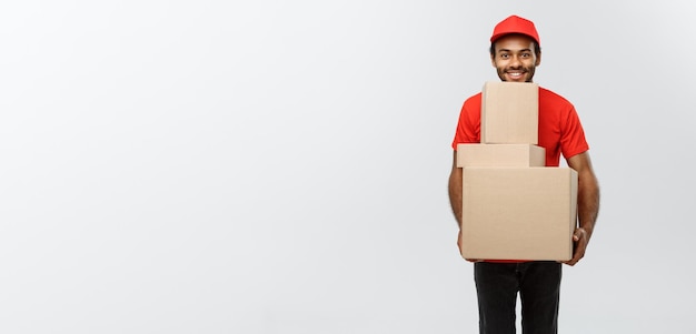 Delivery Concept Portrait of Happy African American delivery man in red cloth holding a box package Isolated on Grey studio Background Copy Space