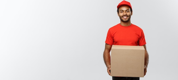 Delivery concept portrait of happy african american delivery man in red cloth holding a box package