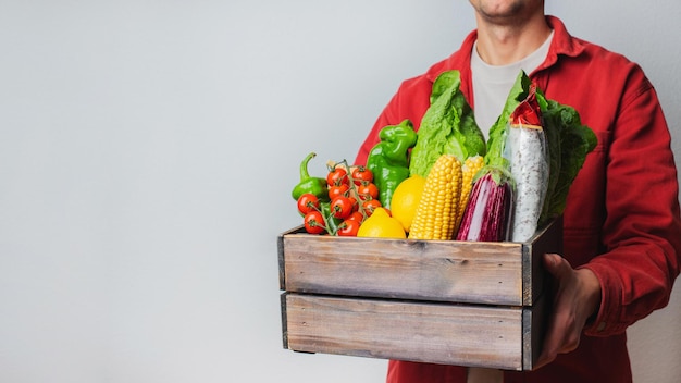 Delivery Concept -Young Caucasian delivery man carrying wooden box of grocery vegetables and fruits from store. Isolated on Grey studio Background. Copy Space