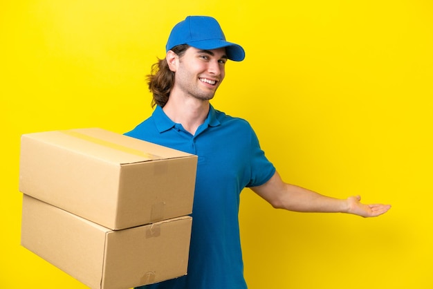 Delivery handsome man isolated on yellow background extending hands to the side for inviting to come