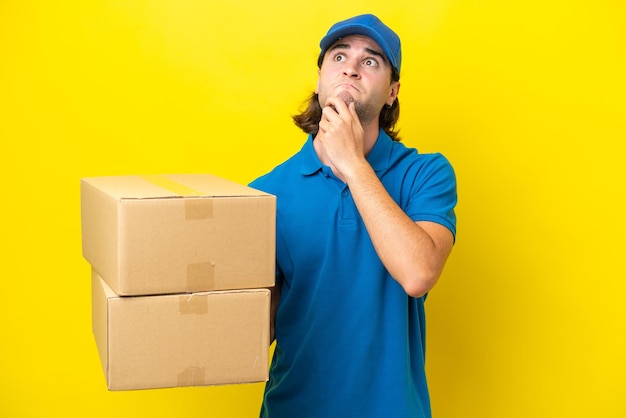 Delivery handsome man isolated on yellow background having doubts and thinking