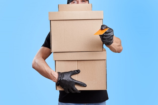 Delivery man in black uniform with medical gloves and protective mask hold cardboard box