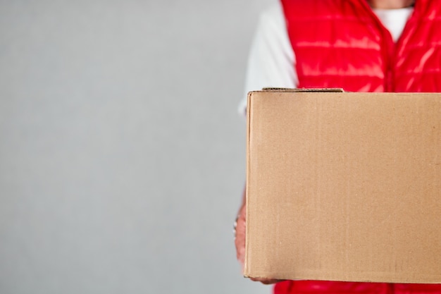 Delivery man employee in red vest uniform hold empty cardboard box isolated