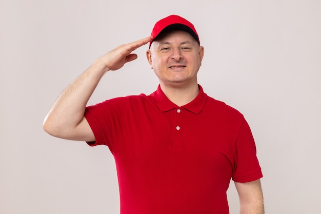 Delivery man in red uniform and cap looking smiling confident saluting