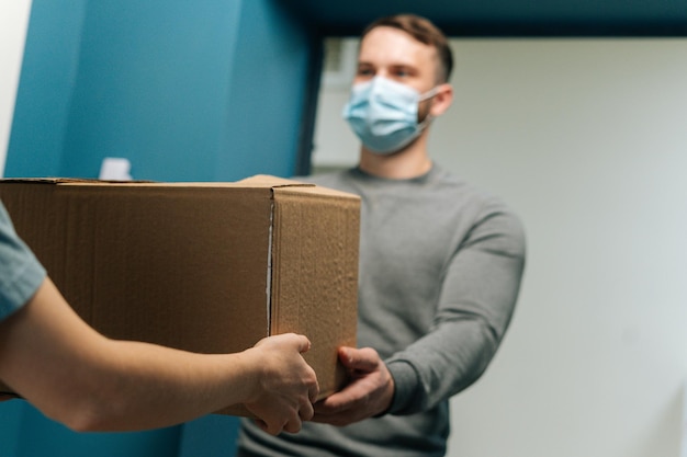 Delivery man wearing medical face mask giving cardboard box parcel to female customer on doorstep at home