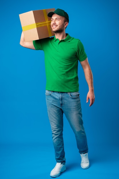 Delivery man with box in studio against blue background