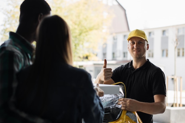 Delivery man in yellow uniform delivering parcel box to recipient young woman and her husband