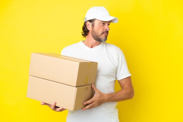 Delivery senior dutch man isolated on yellow background looking to the side