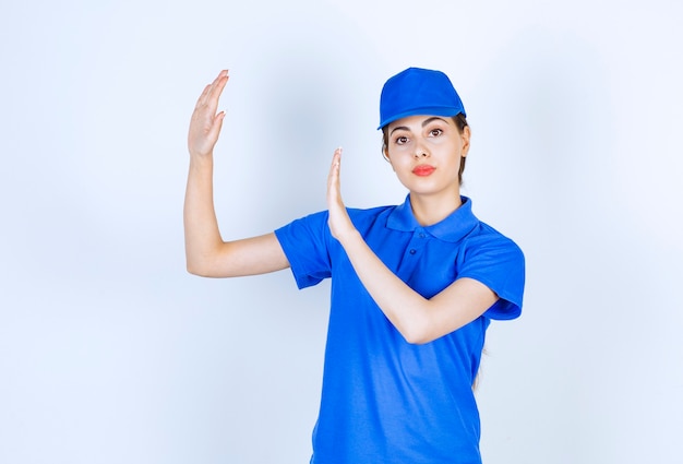 Delivery woman employee in blue uniform standing and showing stop sign .