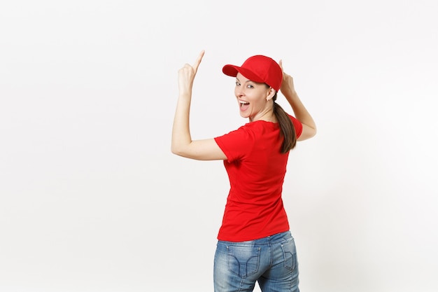 Delivery woman in red uniform isolated on white background. Professional pretty female in cap, t-shirt, jeans working as courier or dealer, pointing fingers on copy space for advertisement. Back view.