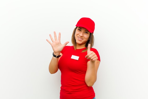 Delivery woman smiling and looking friendly, showing number six or sixth with hand forward, counting down against white 