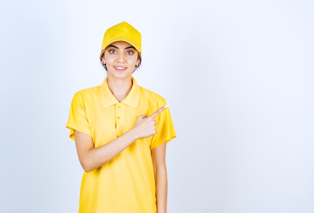 Delivery woman in yellow uniform standing and pointing away with an index finger .