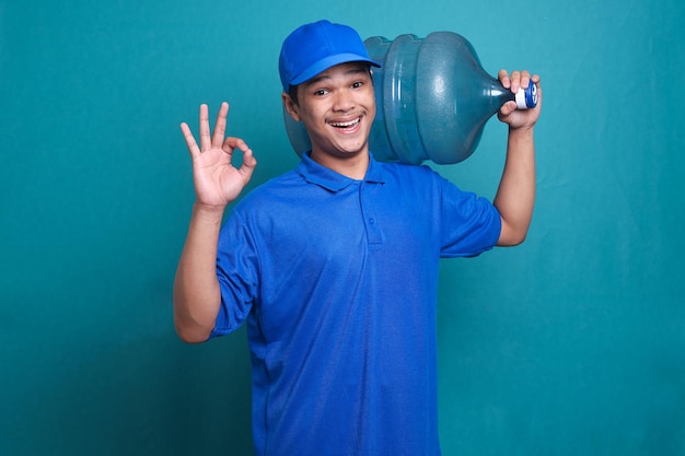 Deliveryman in blue uniform carrying a water gallon and showing okay sign gesture