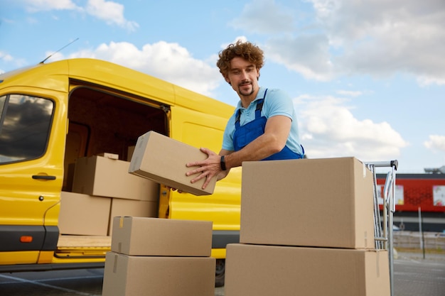 Deliveryman stacking parcel boxes into trolley cart providing courier service