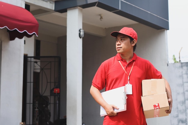 Deliveryman wearing red uniform holding stack of cardboard and document on clipboard outdoor