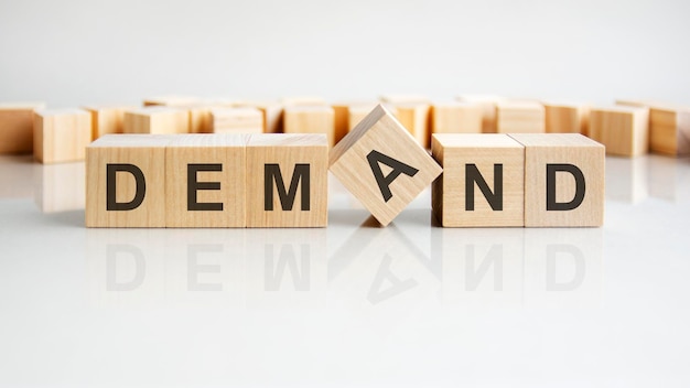 Demand word of wooden blocks with letters on a gray background reflection of the caption on the mirrored surface of the table selective focus