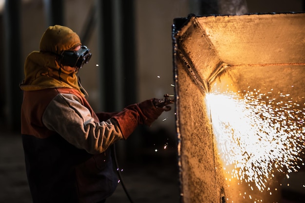 Demolition construction worker using a flame torch to cut up heavy machinery