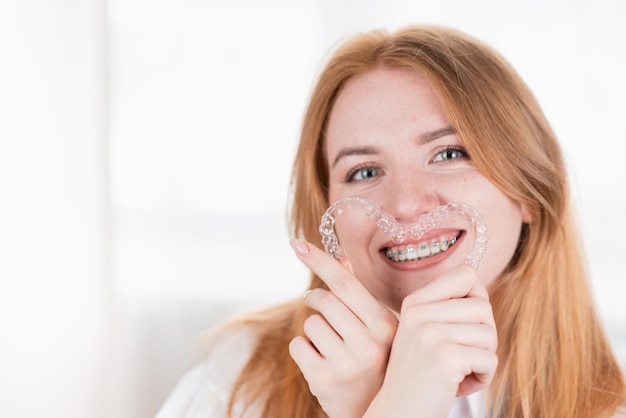 Dental careSmiling girl with braces on her teeth holds aligners in her hands and shows the difference between them