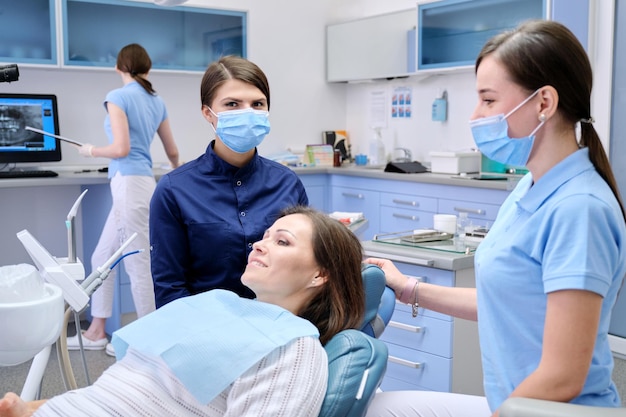 Dental examination, treatment of teeth, patient mature woman in chair and doctor dentist with an assistant. Medicine, dentistry and health care concept