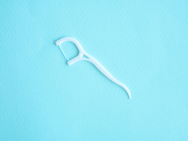 Dental floss with white plastic toothpick on blue with space for text Dental concept