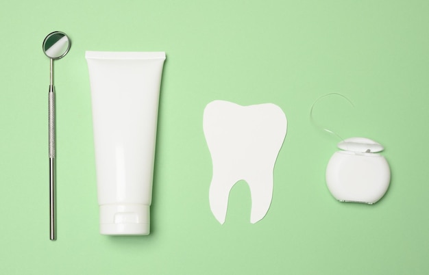 Dental mirror tube of toothpaste and dental floss on a green background