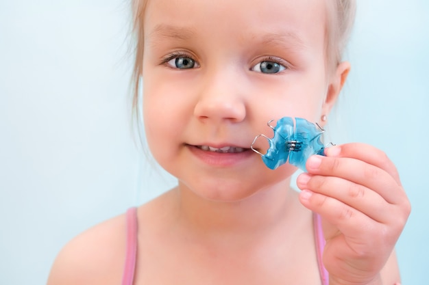 Dental plate. Expansion of the jaw in a child. A plate to heaven. There is not enough room for the molars. Happy girl holding an orthodontic plate in her hands